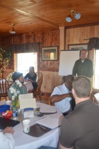 Blaine Alexander (Arkansas Leadership Academy) (standing) facilitates leadership building session. Leadership participants Landon Downing (Lyon College) (left), Calvin Taylor (Ambassador Services) (center), and Kenny Rains (LaCroix Optical) (right) prepare for a team activity.